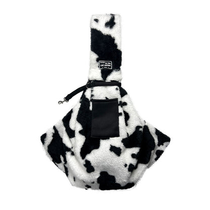 Front of the cow-print pet sling showing its shoulder strap and pocket
