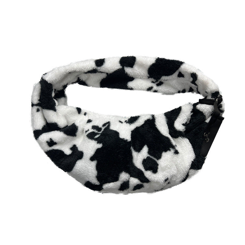 Side view of the cow-print pet sling showing the shoulder strap and pouch